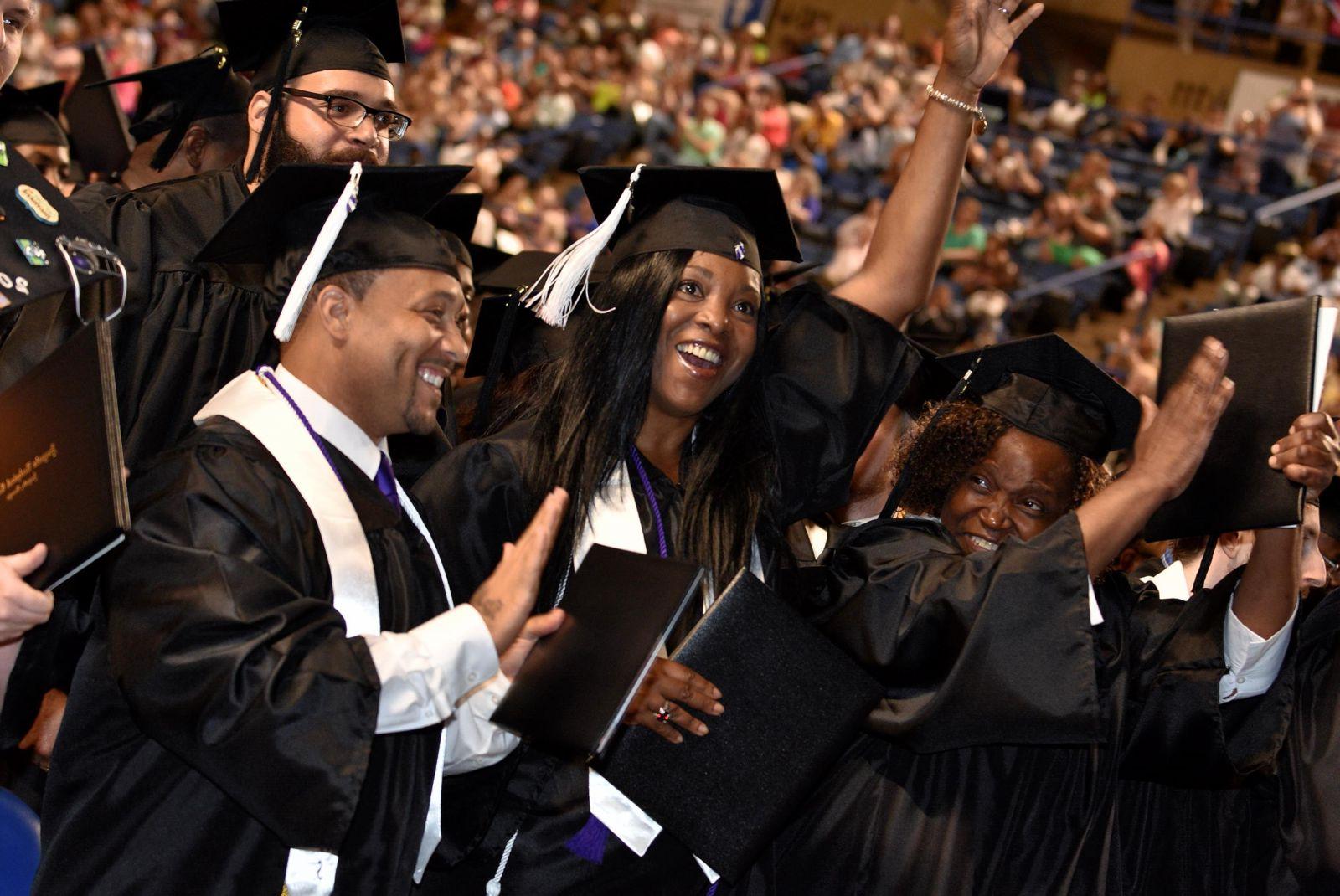 A forest green, hyperlinked, 白色的技术信用证书按钮, bolded, 在文字下面加了下划线，上面是一群拥挤的毕业生和家人，他们的注意力集中在四名戴着黑色毕业帽、穿着白色流苏长袍和披肩的毕业生身上:一名非洲裔美国女性微笑着，左手举着一个黑人文凭/学位托, 在她的左边，一位非洲裔美国女性微笑着举起戴着金属手镯的右手，左手拿着她的黑人学位证书, 一位非裔美国男性微笑着站在那里，右手拿着他的黑人文凭/学位证书，左手举在后面, 一个留着黑胡子戴着眼镜的白人男性站在他们三人的右边.
